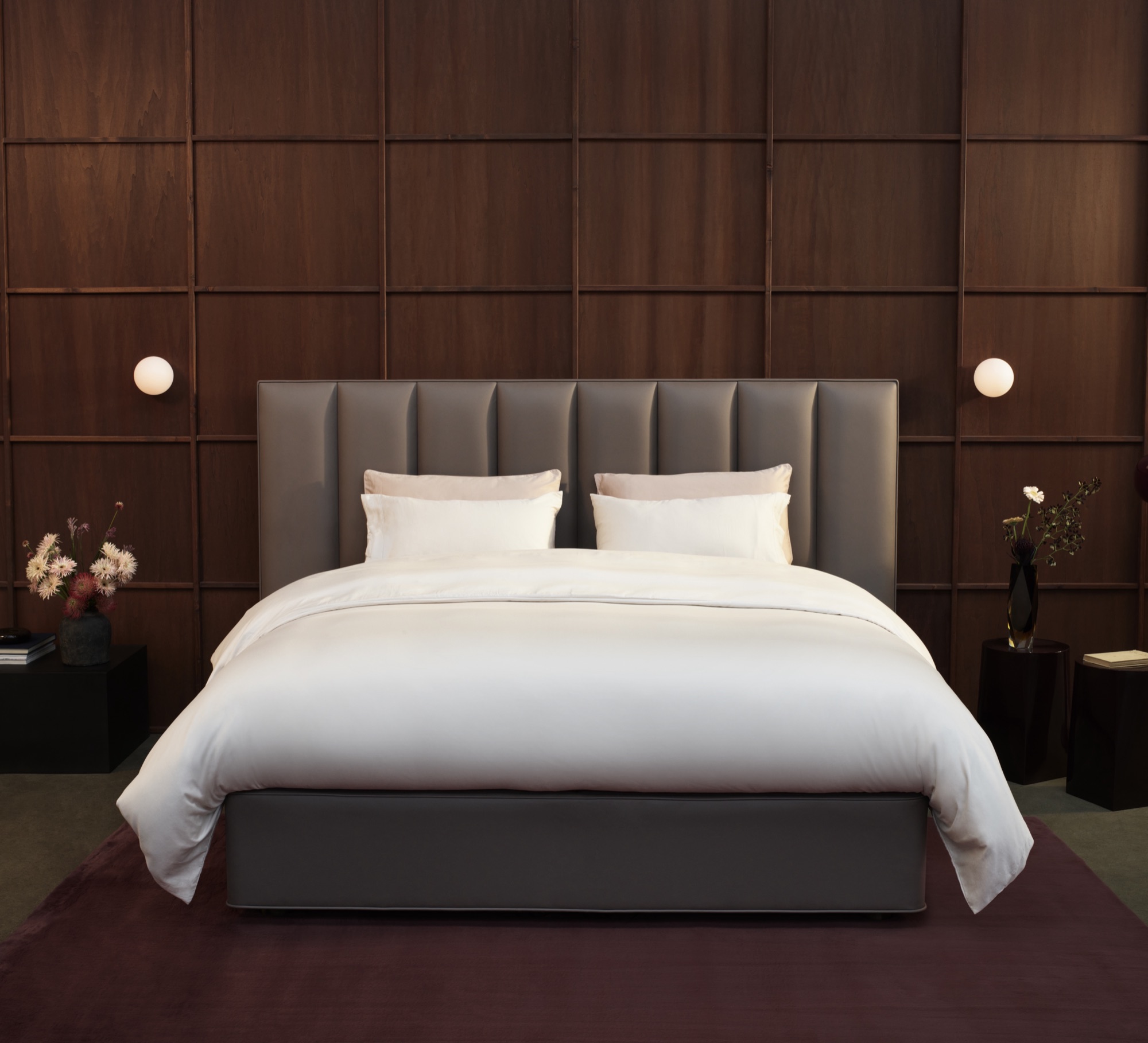 Vispring Luxe Kollektion: Bett mit taupefarbenem Kopfteil vor dunkler Holzvertäfelung